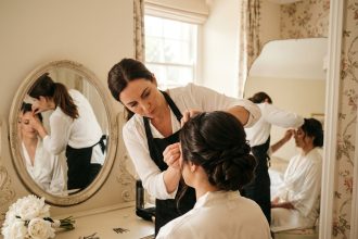 Coiffeuse à domicile réalisant une coiffure de mariée élégante devant un miroir vintage dans une chambre décorée